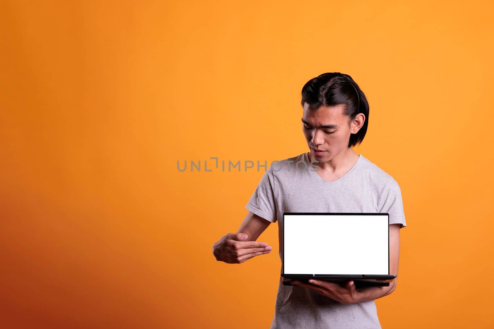 Confident asian man pointing at laptop with blank screen by DCStudio