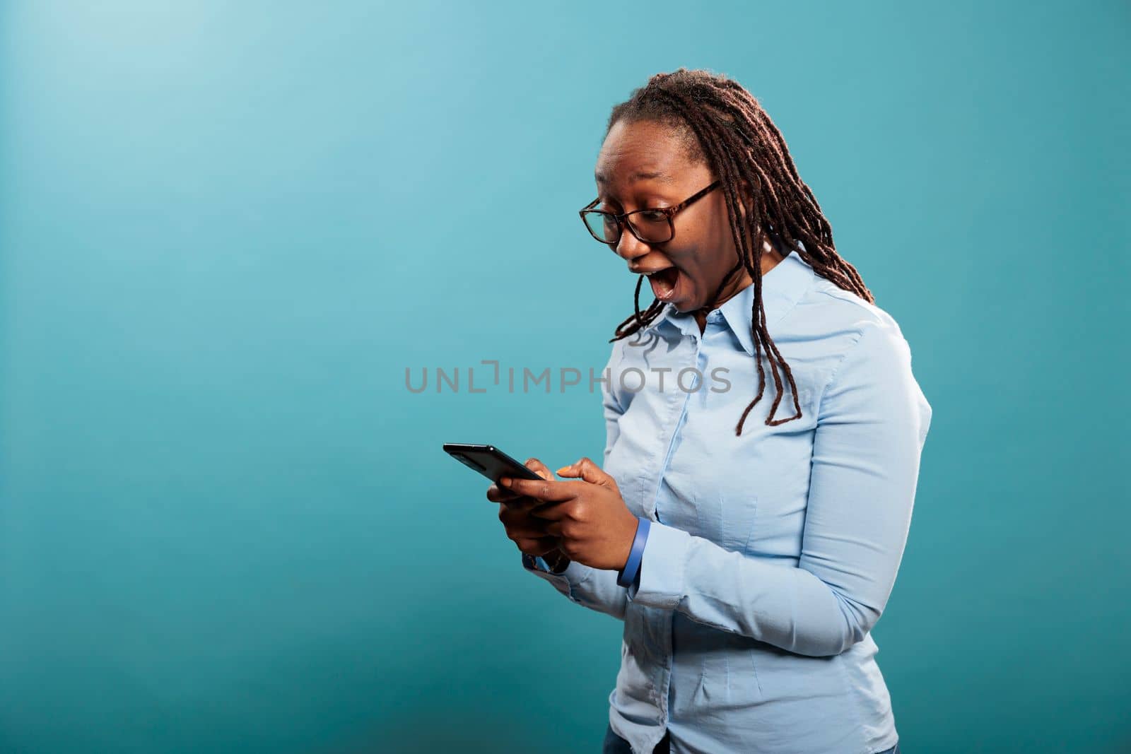 Cheerful excited african american person with smartphone device surprised by received email. Joyful smiling young woman with modern cellphone astonished by social media post reach.