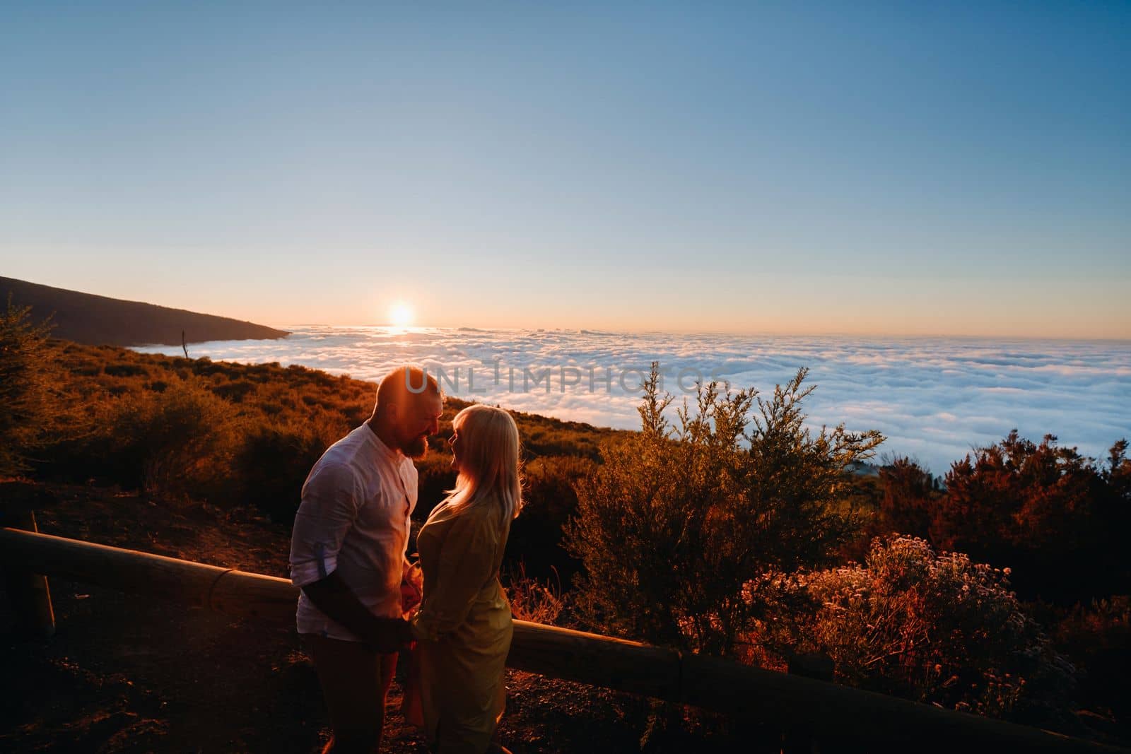 A couple in love hugs at sunset above the clouds on the island of Tenerife, Spain by Lobachad