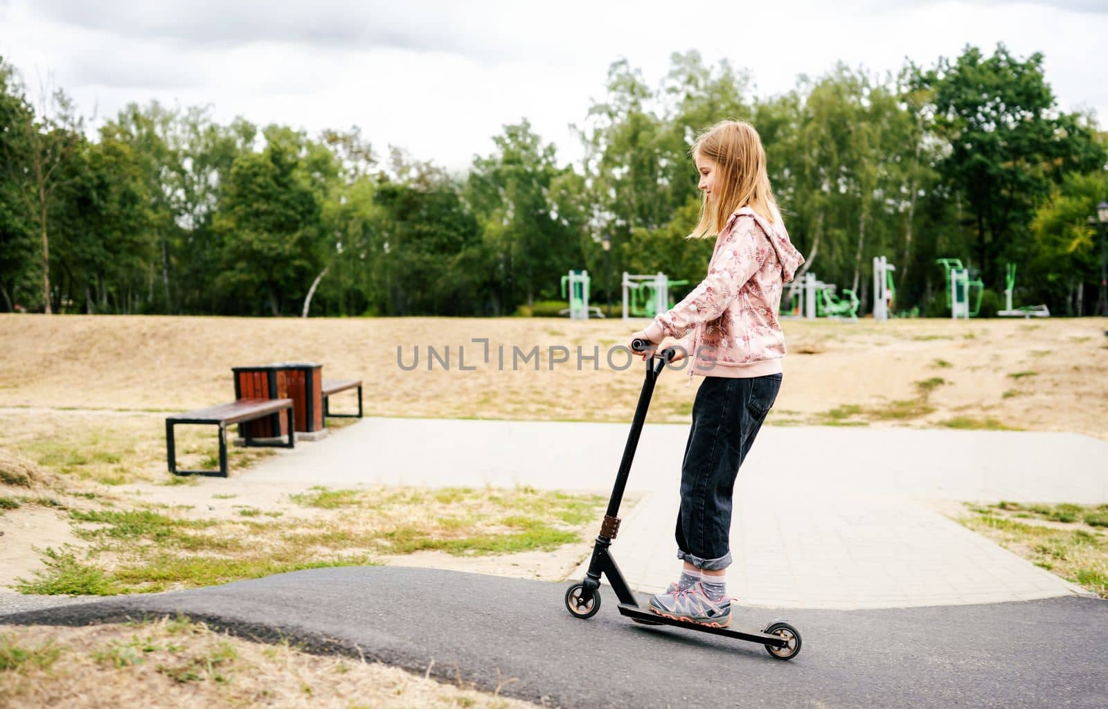 Preteen girl riding scooter in the park. Cute female child with eco vehicle outdoors