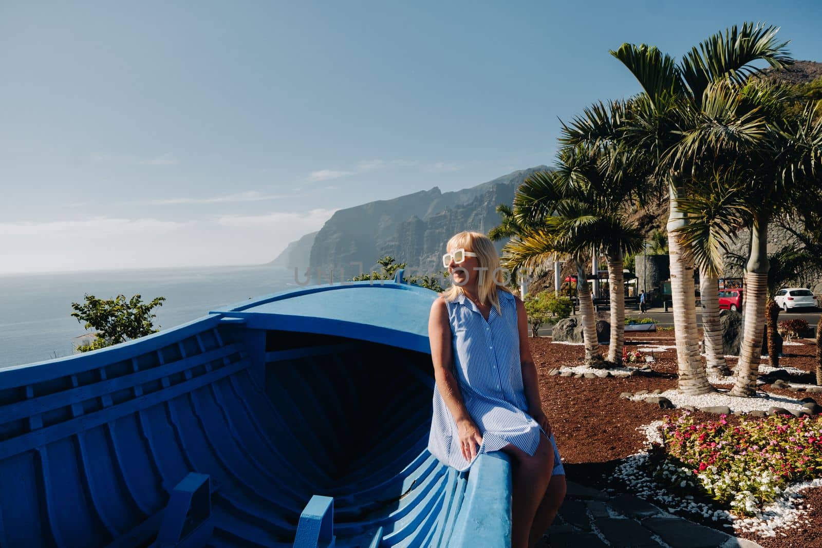 A girl sits on an observation deck against the backdrop of the Acantilados de Los Gigantes mountains at sunset, Tenerife, Canary Islands, Spain.