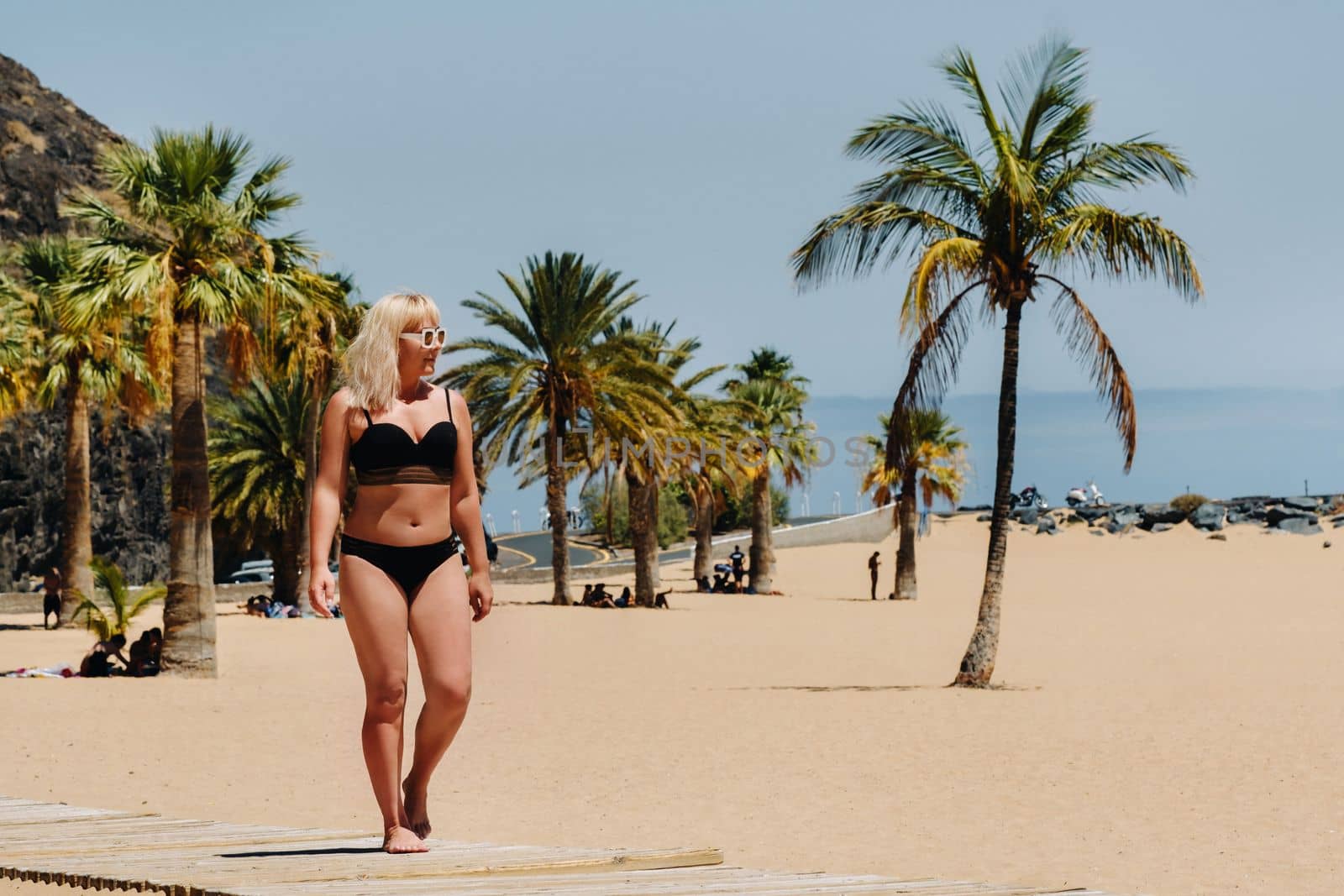 A girl in a black swimsuit walks along the beach of Las Teresitas on the island of Tenerife. The Canary Islands. Spain.