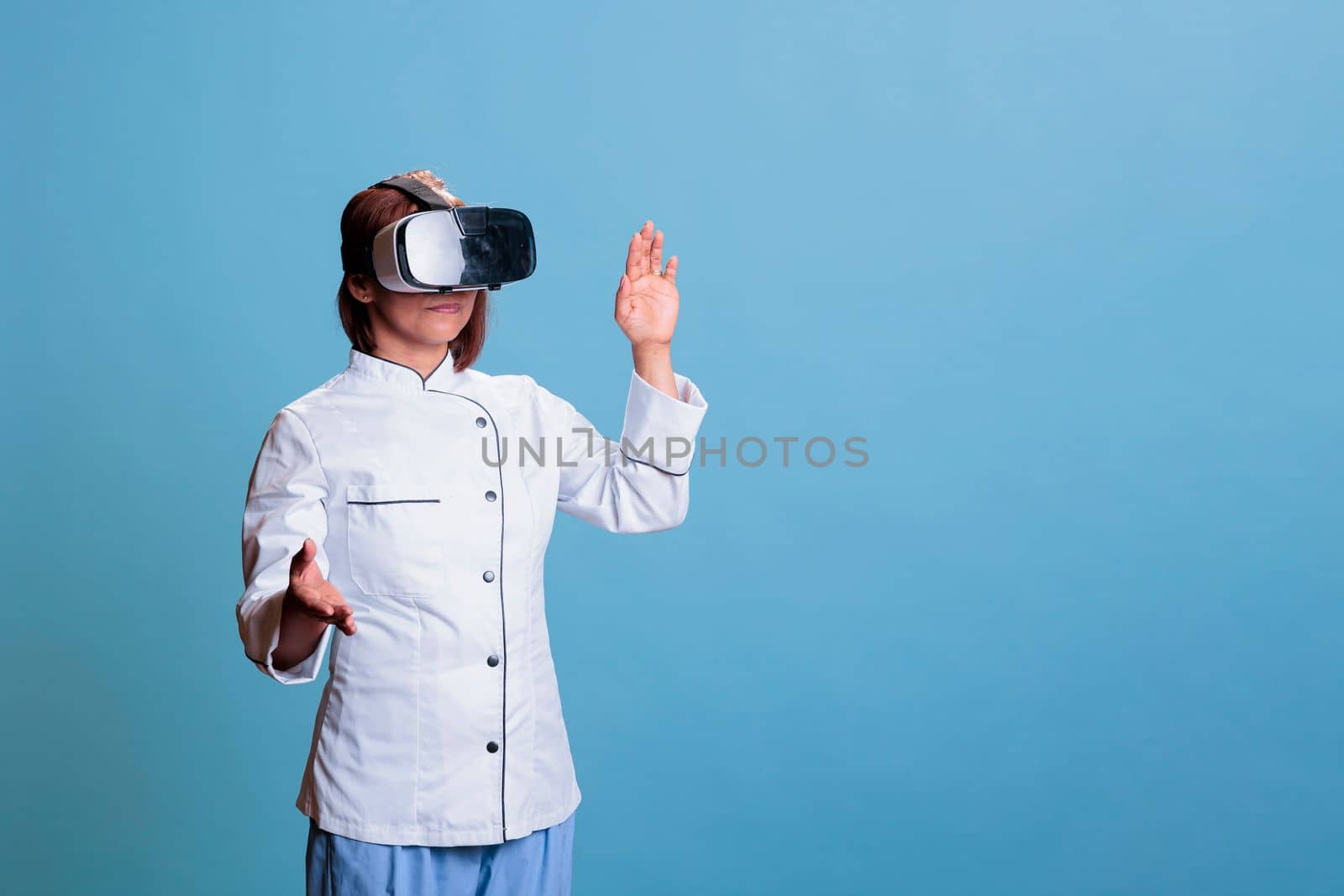 Positive senior cook wearing virtual reality goggles while preparing culinary meal working at healthy recipe. Friendly chef with restaurant uniform cooking gastronomy food dish. Food industry