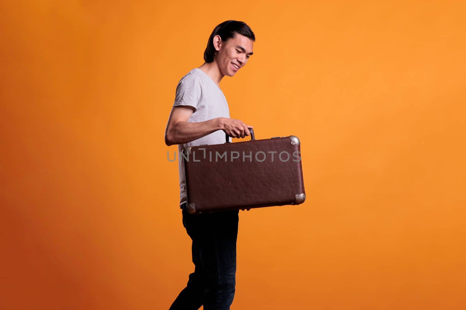 Happy young asian traveler holding suitcase, traveling, tourism concept. Cheerful smiling man standing with baggage, tourist walking with luggage, going on vacation, journey