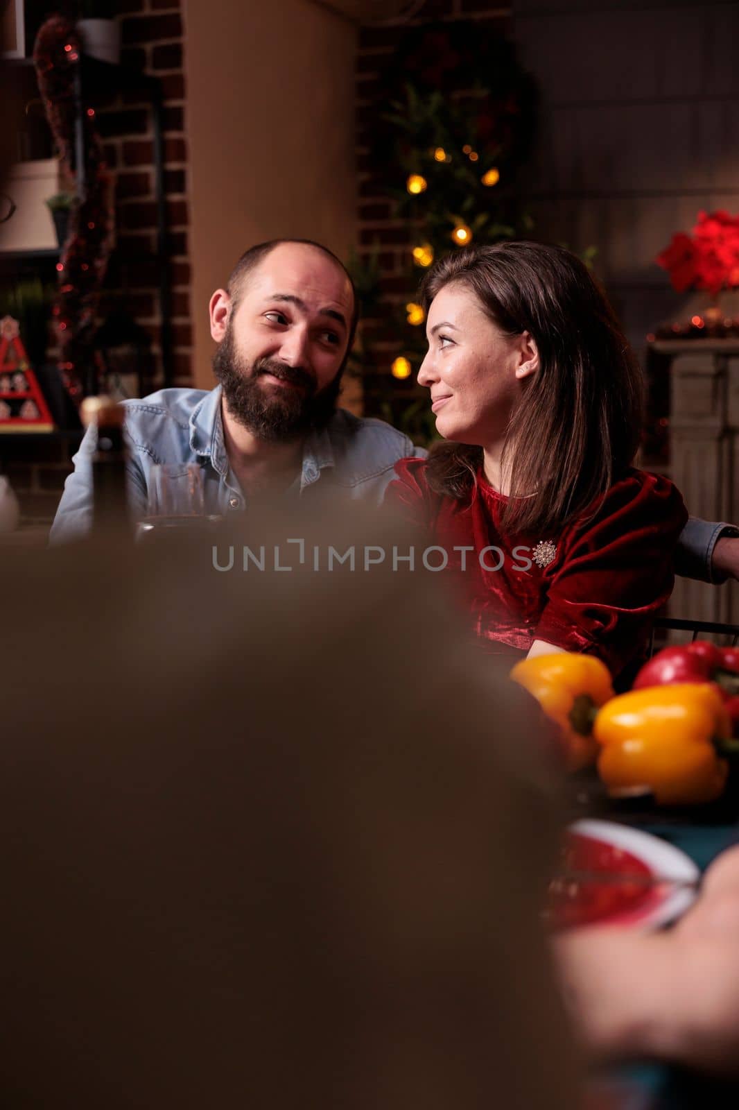 Smiling couple celebrating christmas at decorated home with warm evening candlelight, wife and husband at festive dinner. Xmas celebration with family, people gathering at table