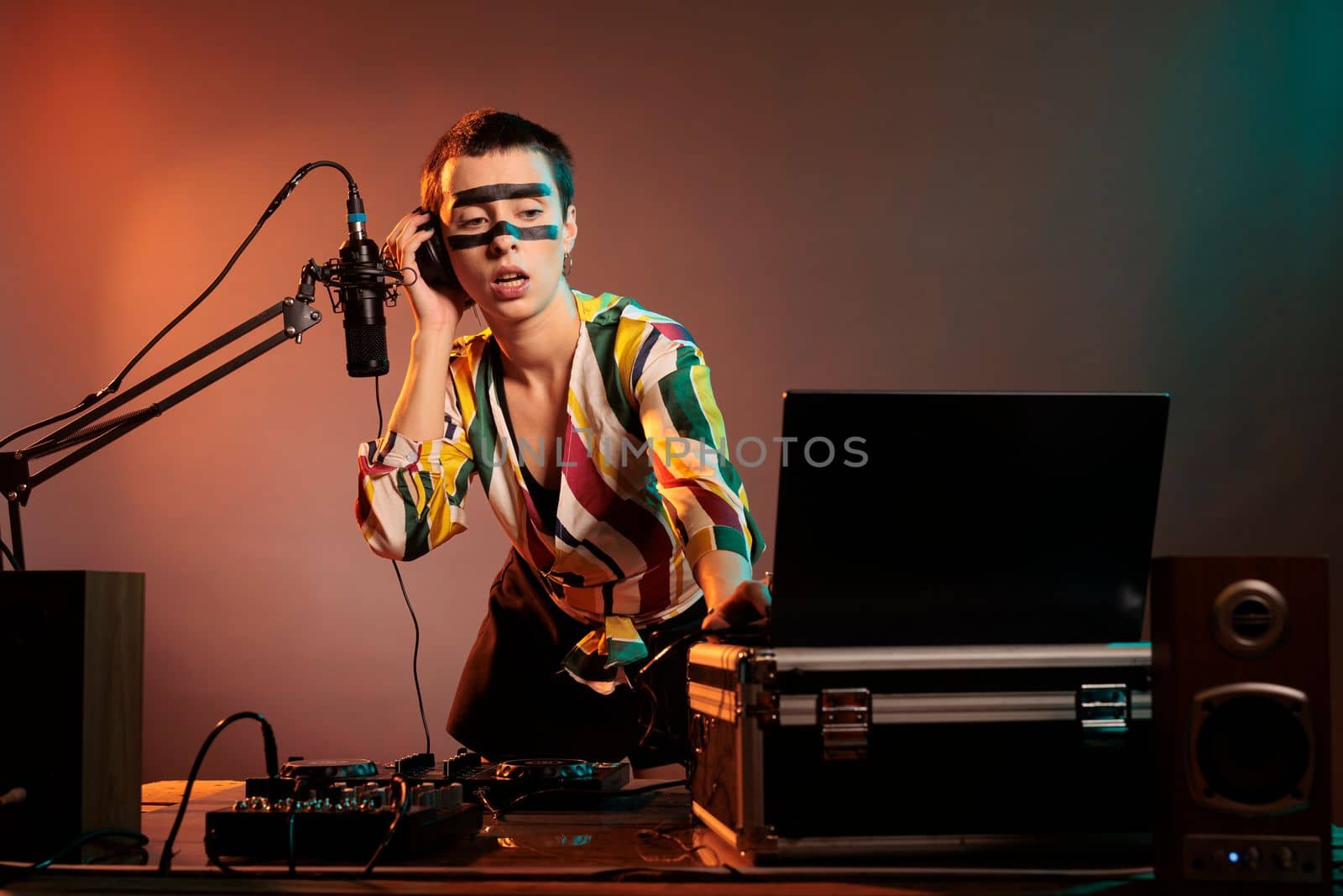 Happy musician playing with techno music on mixer, having fun with turntables as disc jockey and mixing sounds in nightclub studio. Using headphones and microphone to test bass control key.