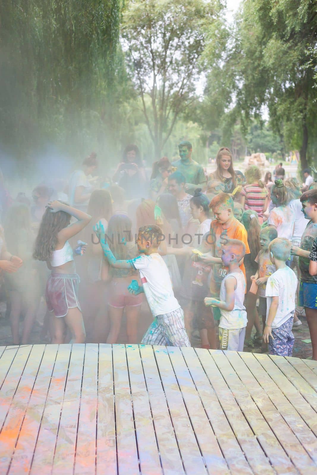 Lviv, Ukraine - July 18, 2021: Color Holi Festival, a crowd of people adults and small children throw colorful paint. Indian holiday, children running on a wooden stage. by sfinks