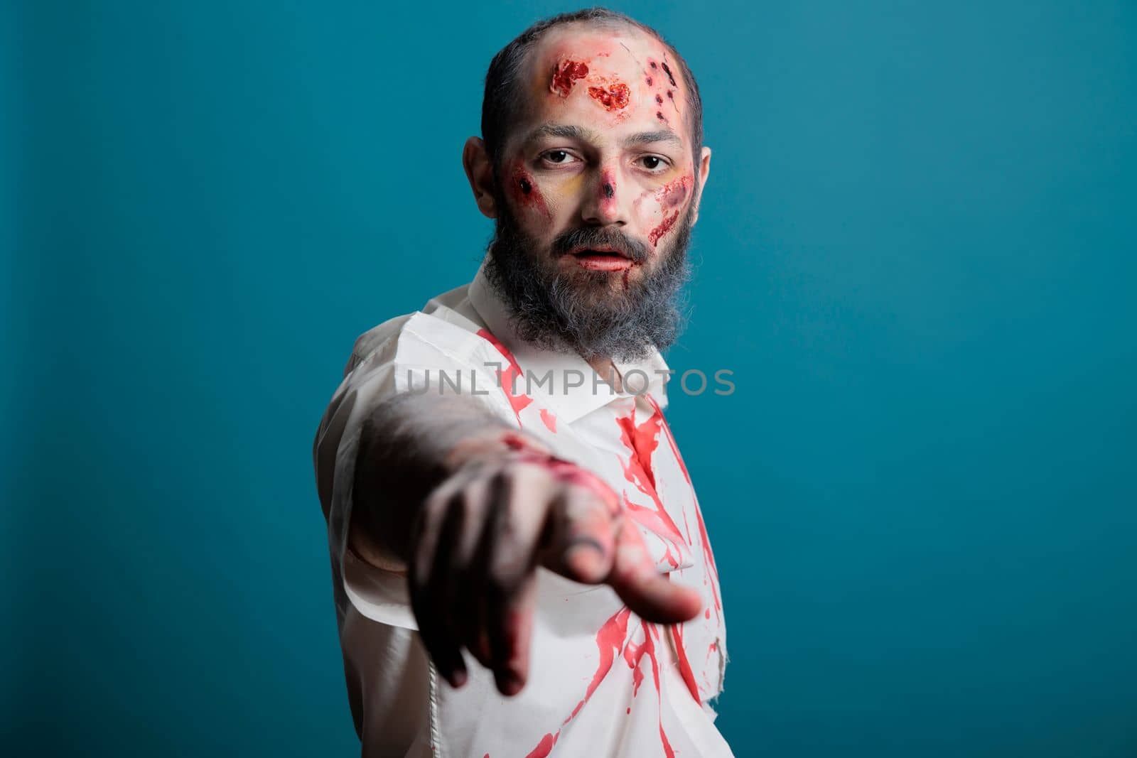 Portrait of halloween zombie posing on camera, looking spooky and dangerous with apocalyptic scars and bloody wounds in studio. Evil aggressive brain eating monster, frightening corpse.