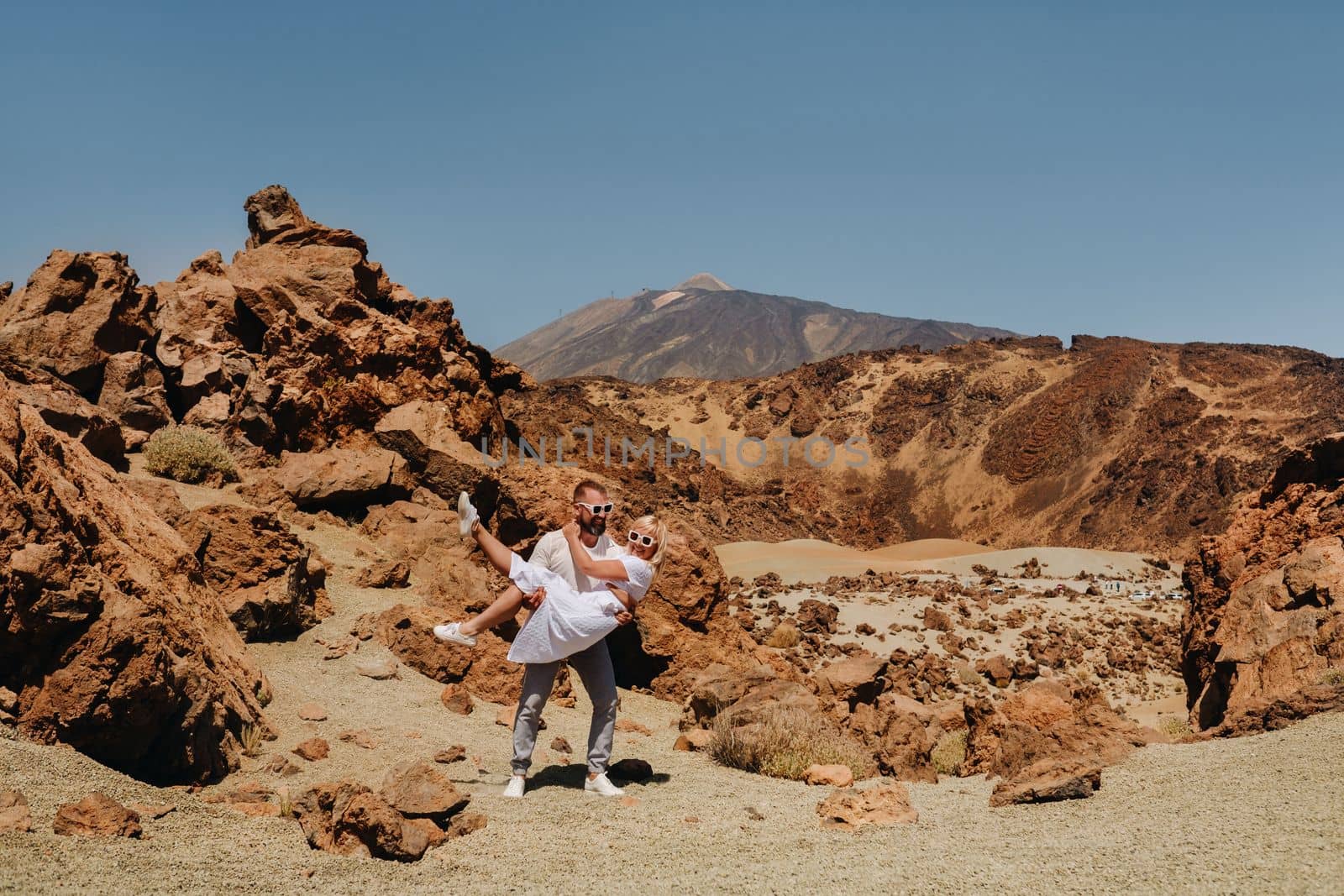 A married couple is standing in the crater of the Teide volcano. Desert landscape in Tenerife. Teide National Park. Tenerife, Spain by Lobachad