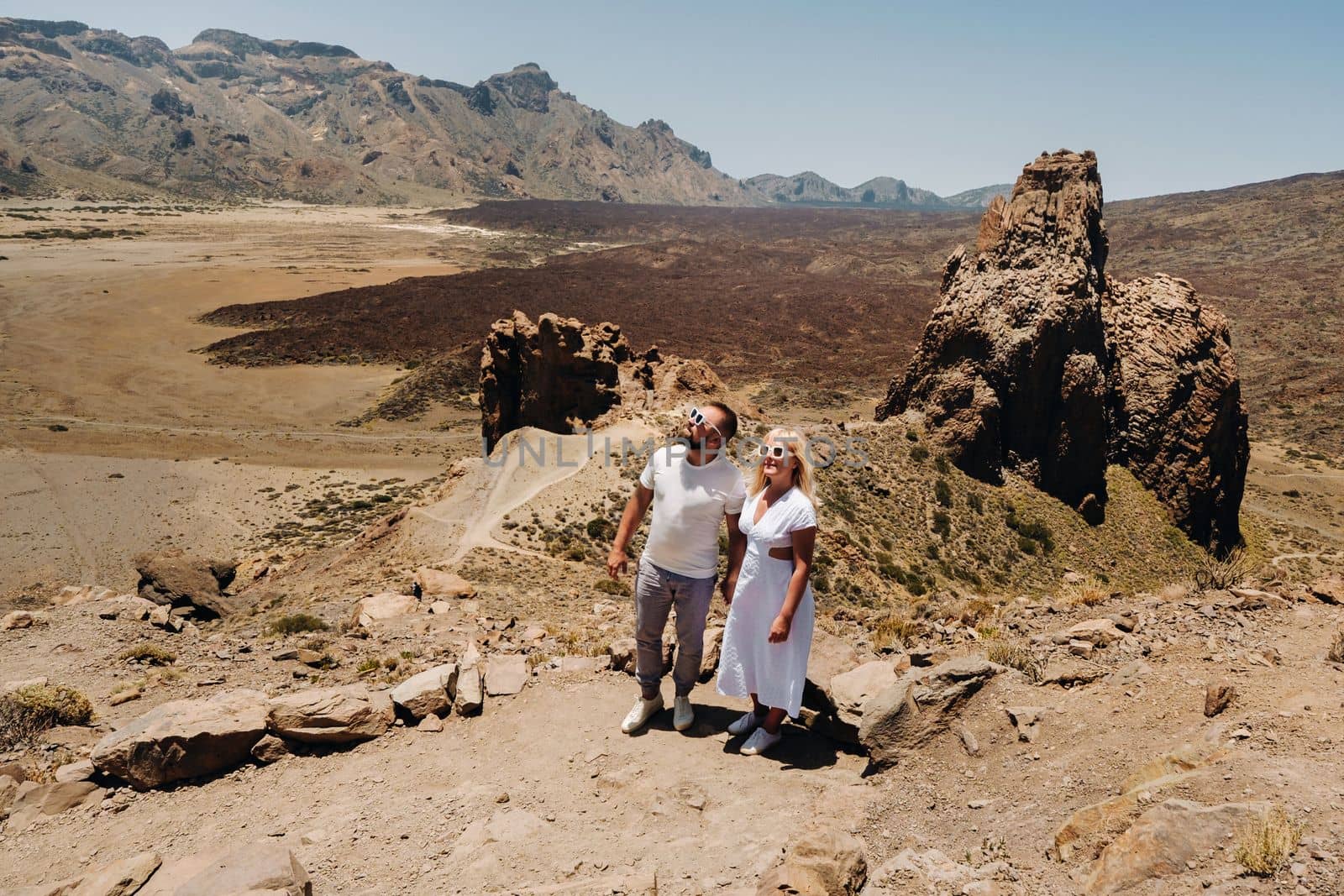 A married couple is standing in the crater of the Teide volcano. Desert landscape in Tenerife. Teide National Park. Tenerife, Spain by Lobachad