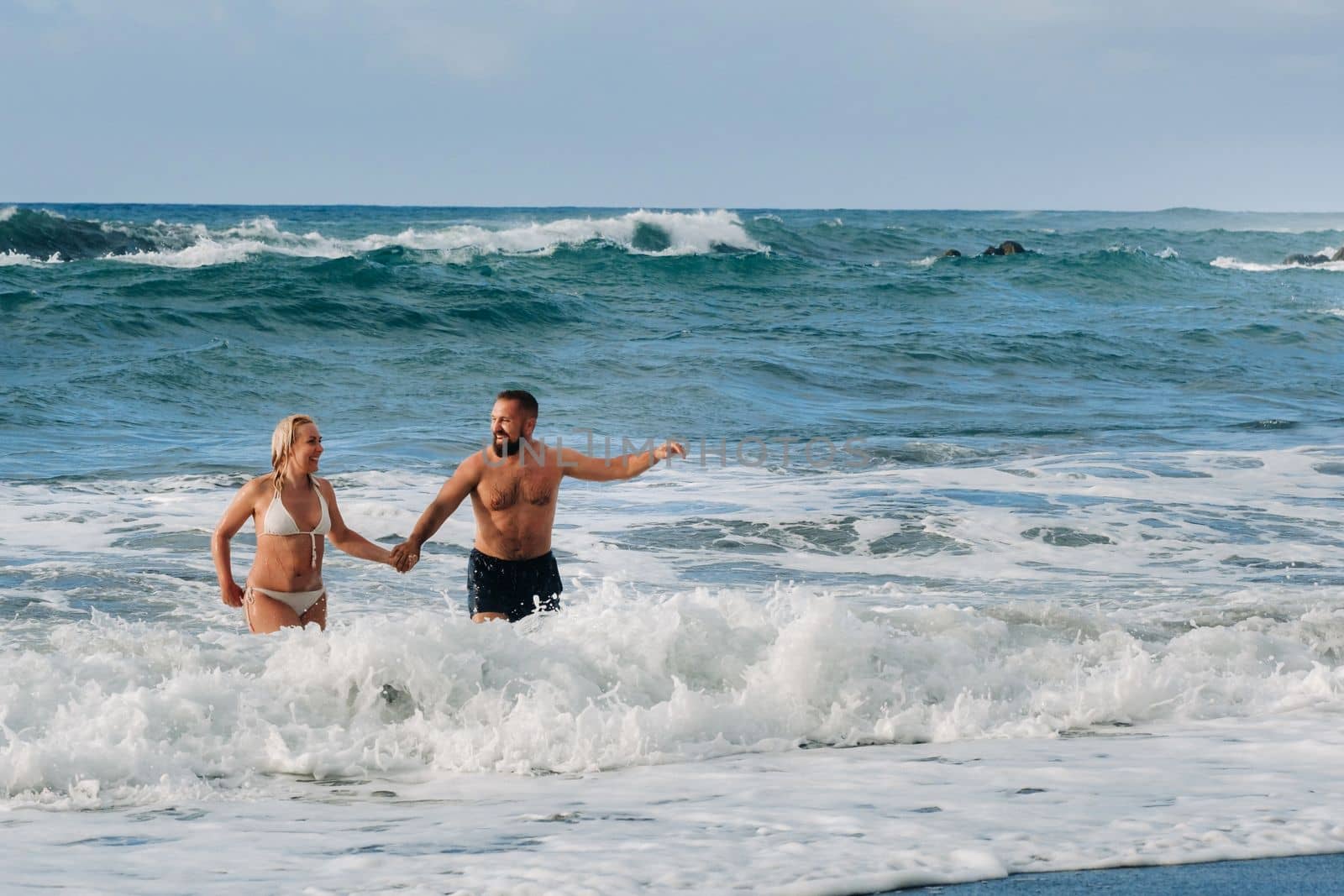 A married couple swims in the sea on the waves, holding hands. The concept of a romantic trip.