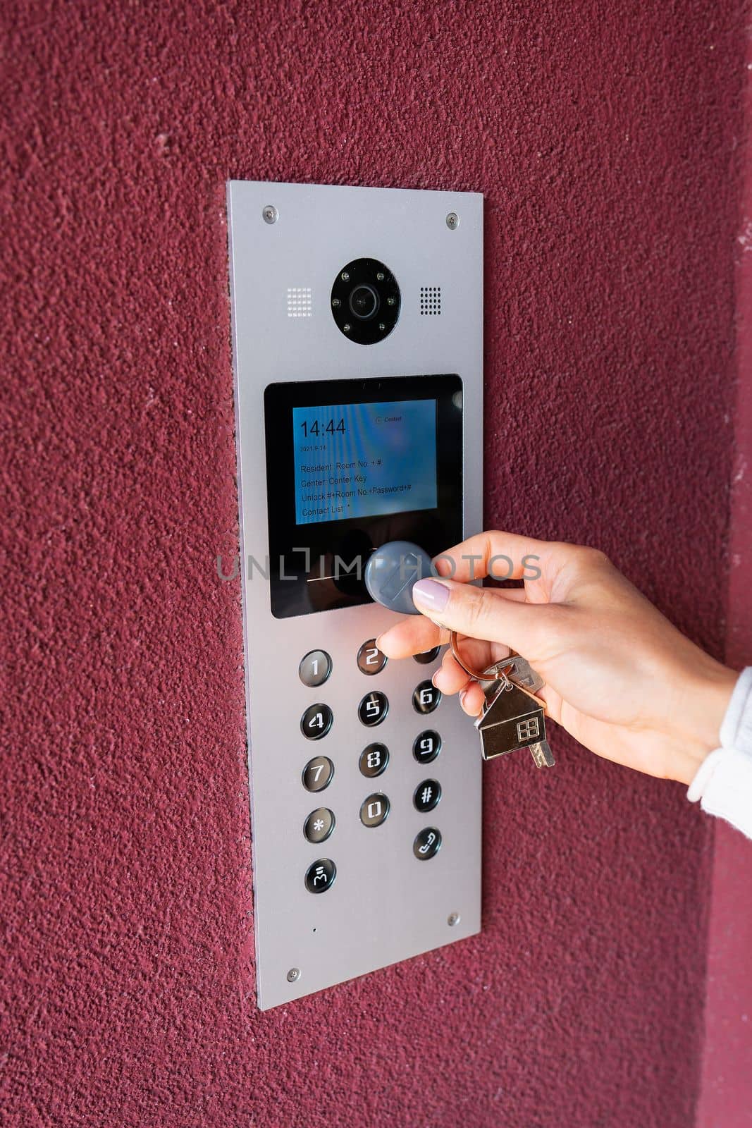 A young woman types the apartment code on the electronic intercom panel, opens the door with a touch key, the screen for viewing information. Protection and security concept. by sfinks
