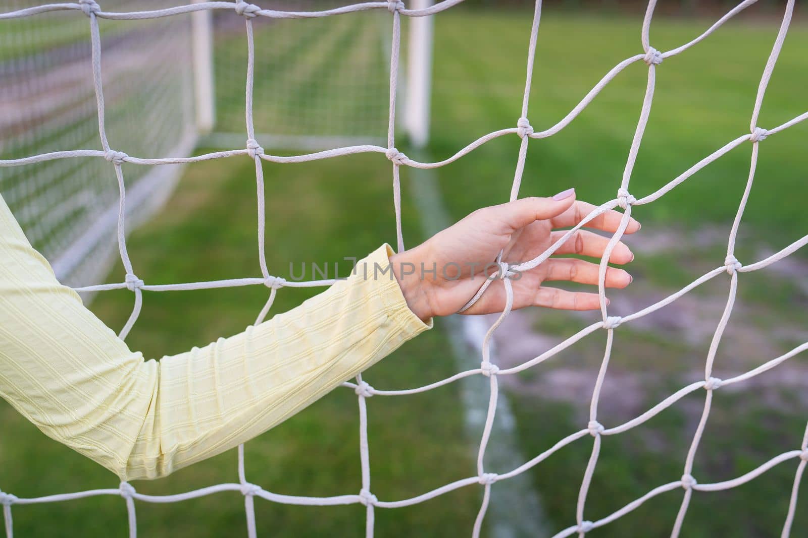 A girl stands near a white net close-up on a soccer field, a soccer goal. Green field. by sfinks
