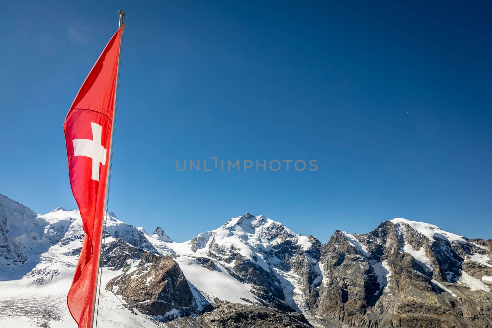 Swiss flag and Bernina mountain range with glaciers in the Alps, Engadine, Switzerland