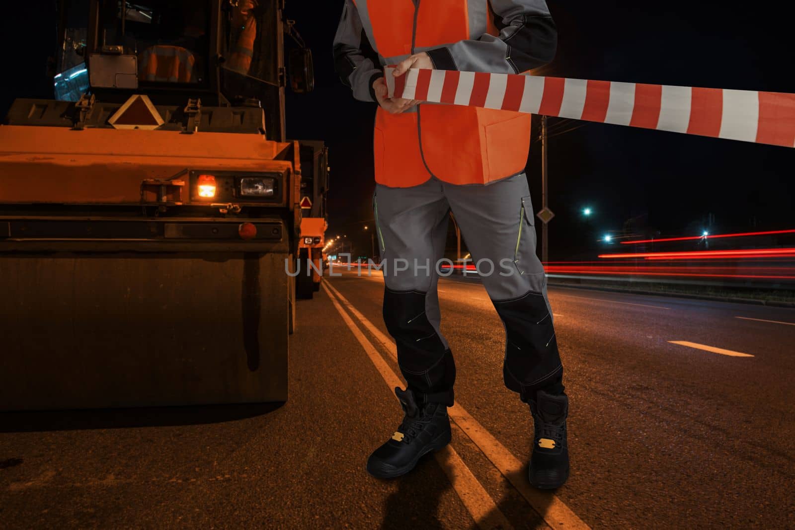 Man in special clothes blocks the road with a tape. Street asphalt resurfacing concept.