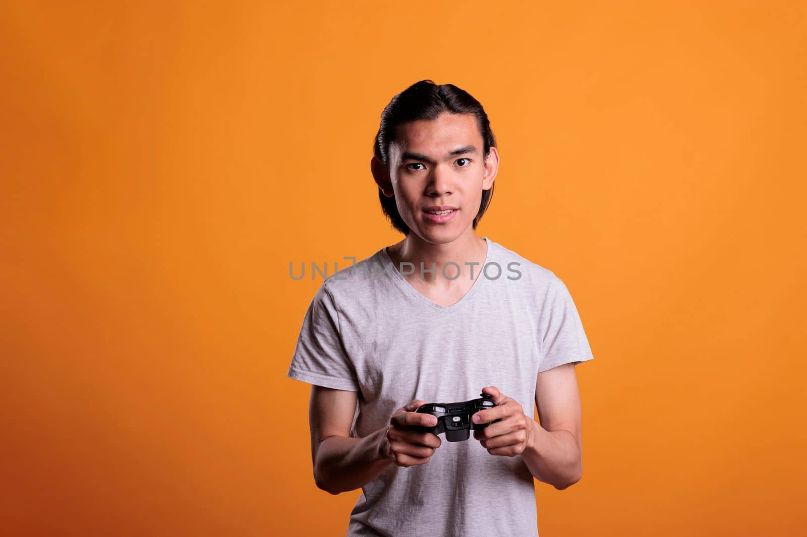 Teenager playing video games with joystick, entertainment activity. Concentrated young asian man holding gamer gadget, person using console wireless controller, enjoying videogames