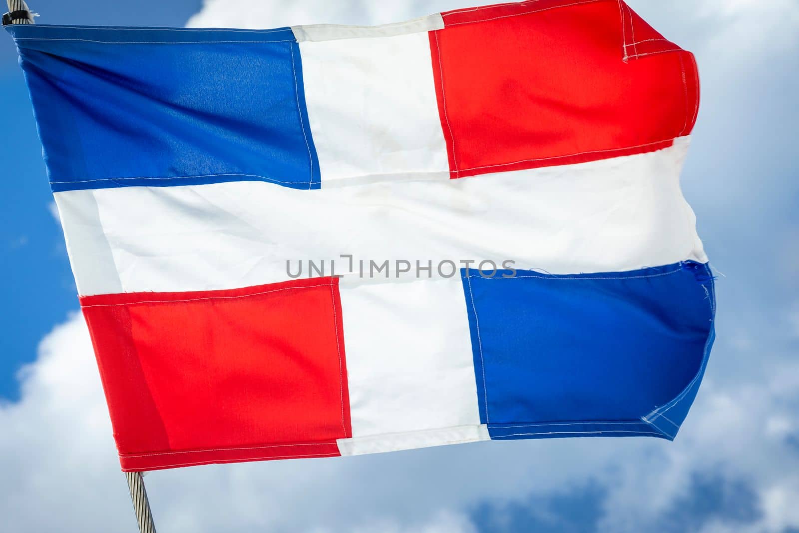 Dominican Republic National Flag Waving on pole against sunny blue sky in Punta Cana