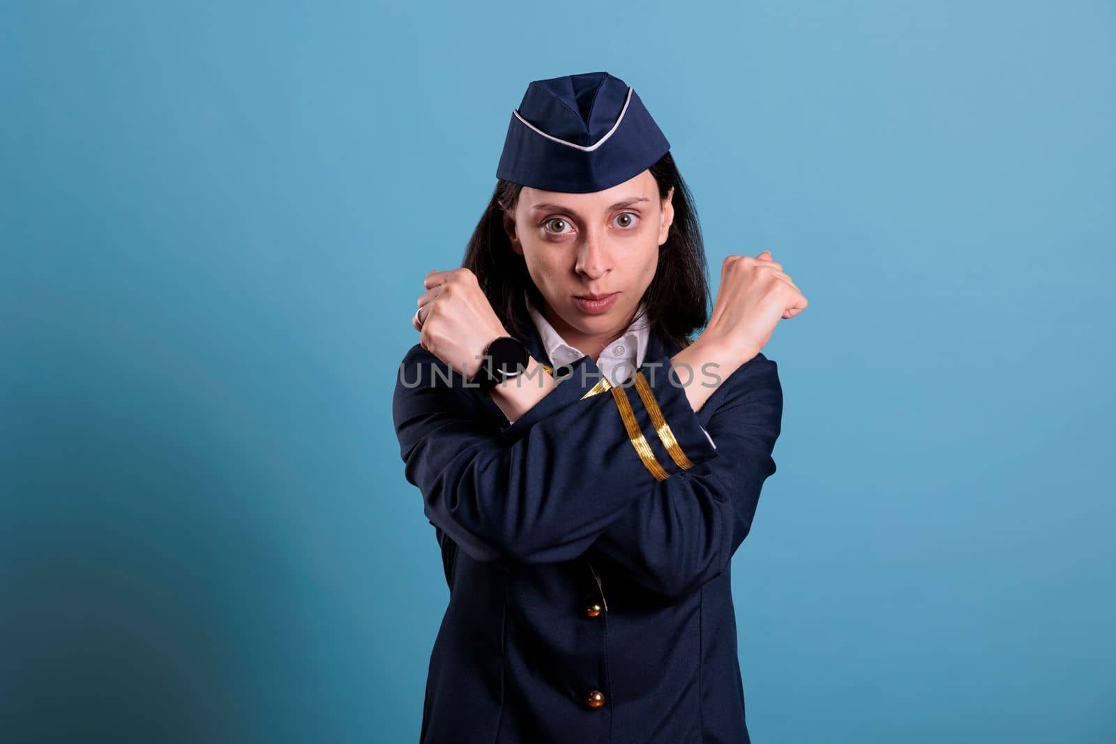 Flight attendant showing stop gesture with crossed arms, clenched fists. Stewardess in uniform looking at camera with serious facial expression, prohibition concept, defense symbol