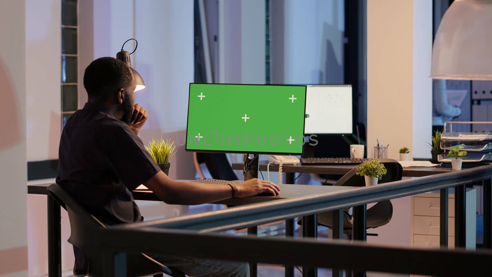 Startup worker analyzing greenscreen on monitor in office with big windows, looking at desktop isolated screen. Working with chroma key display, blank copyspace and mockup template. Tripod shot.