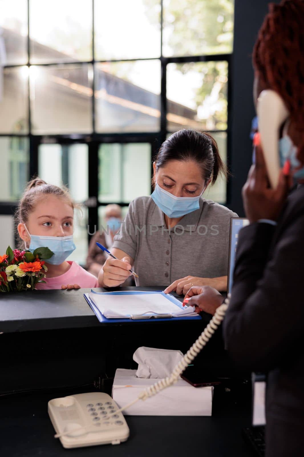 Mother standing at reception with child signing papers with medical insurance during appointment by DCStudio