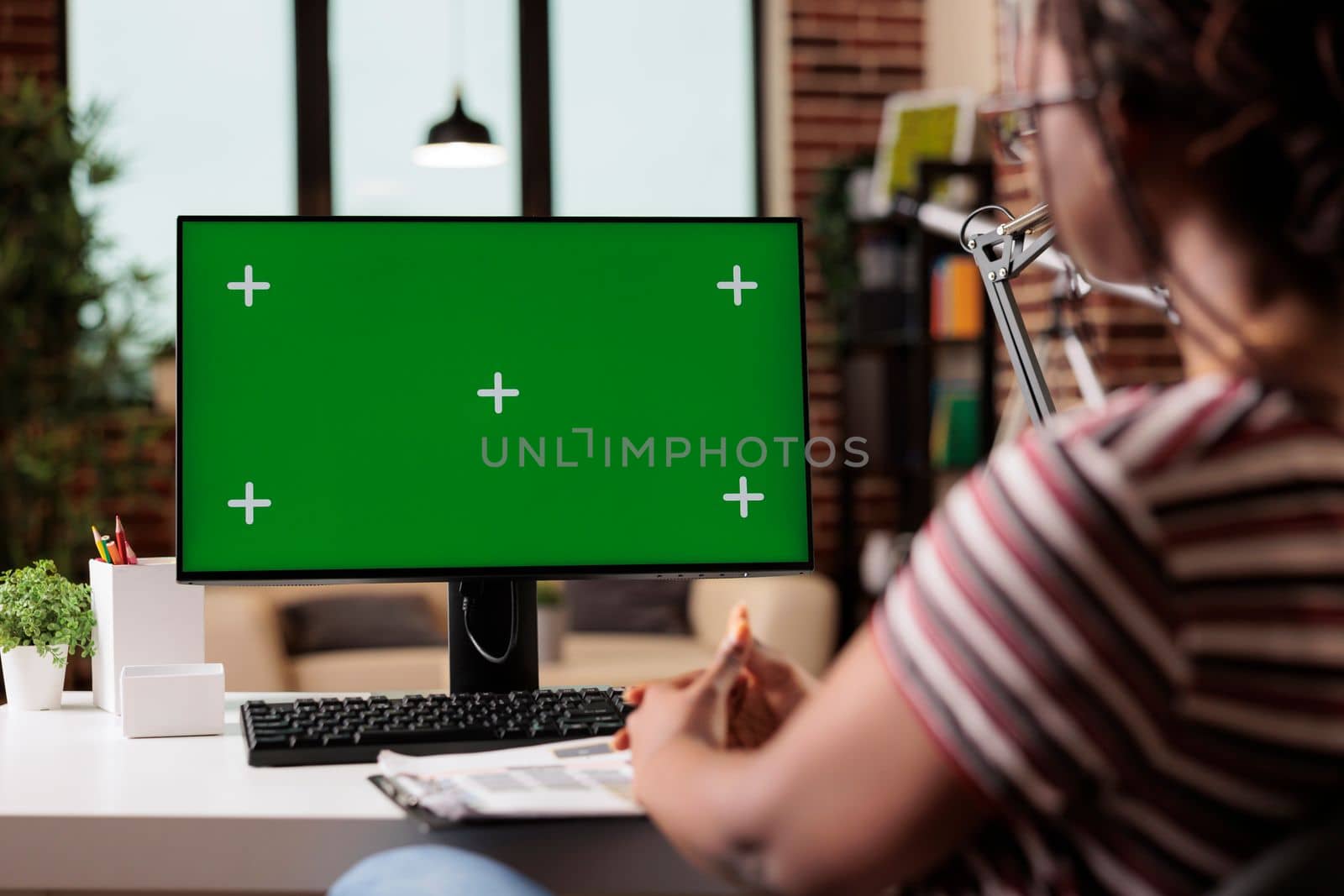 Remote worker computer with green screen at home office table, focus on pc monitor mock up. Woman working, sitting at workplace desk, employee professional equipment with chroma key display
