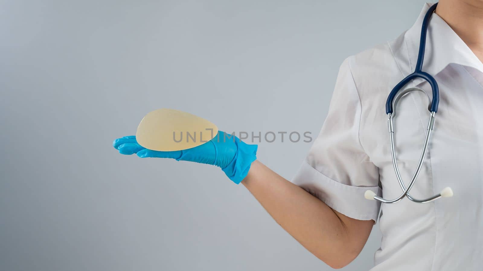 Female doctor aesthetic surgeon holding a breast implant on a white background. by mrwed54