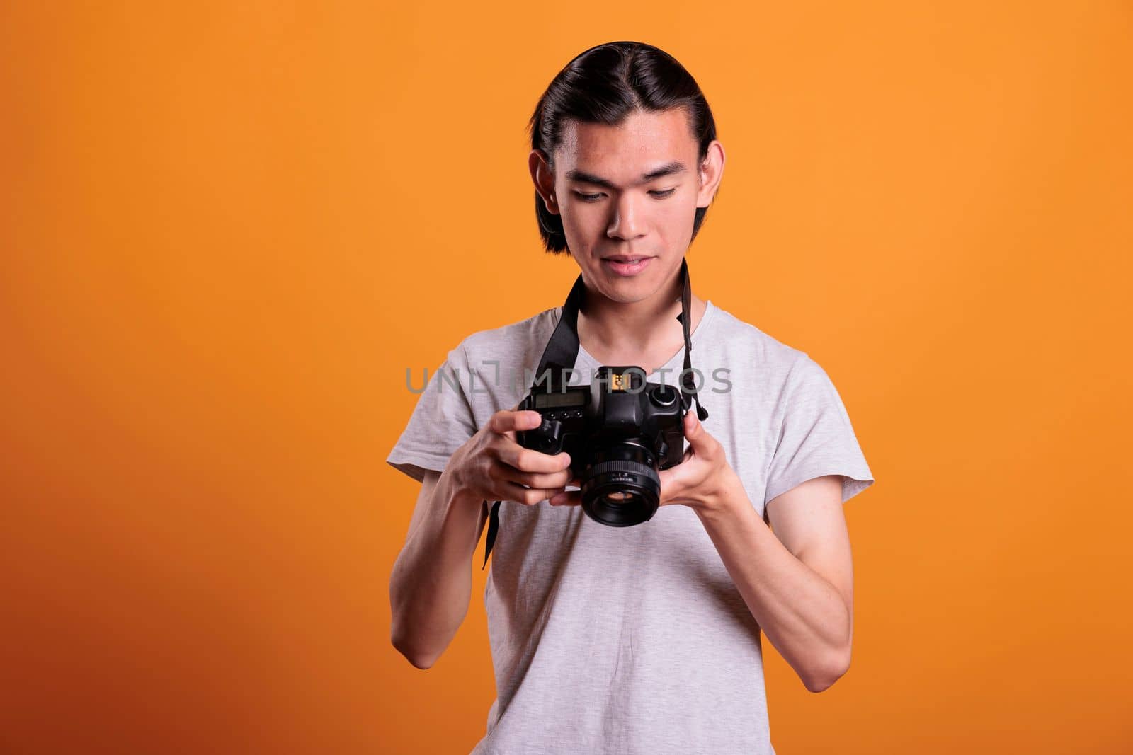 Young photographer taking photos on professional dslr camera, looking at electronics display. Attractive asian man photographing, front view medium shot, creative hobby, photoshoot