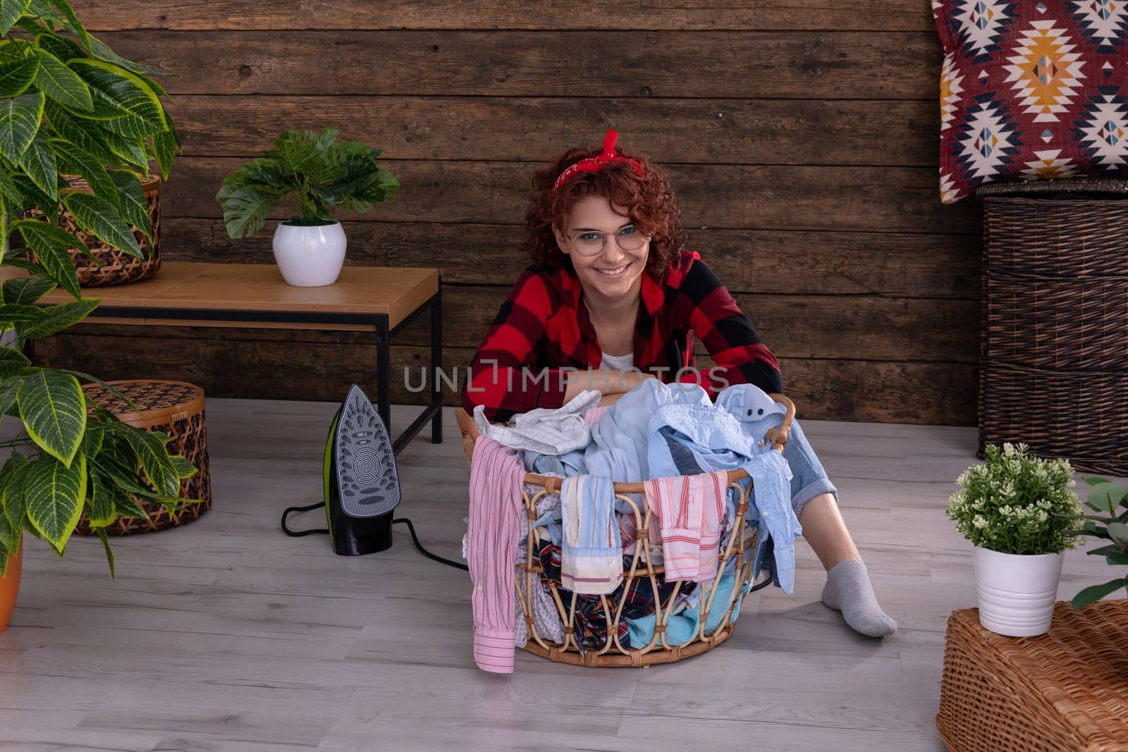 Happy and smiling girl that she will be able to quickly iron clean clothes after washing. Full of vigor and strength to work. A wall in the house made of boards.