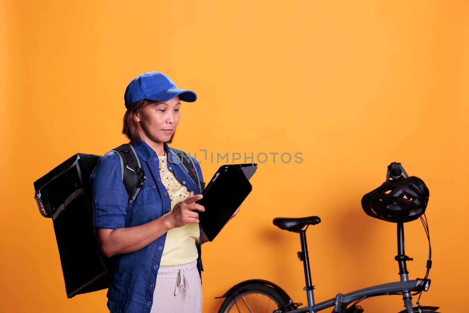 Slide view of cheerful deliverywoman holding tablet computer checking client location to deliver takeaway pizza. Restaurant courier carrying takeout food backpack. Food service and transportation