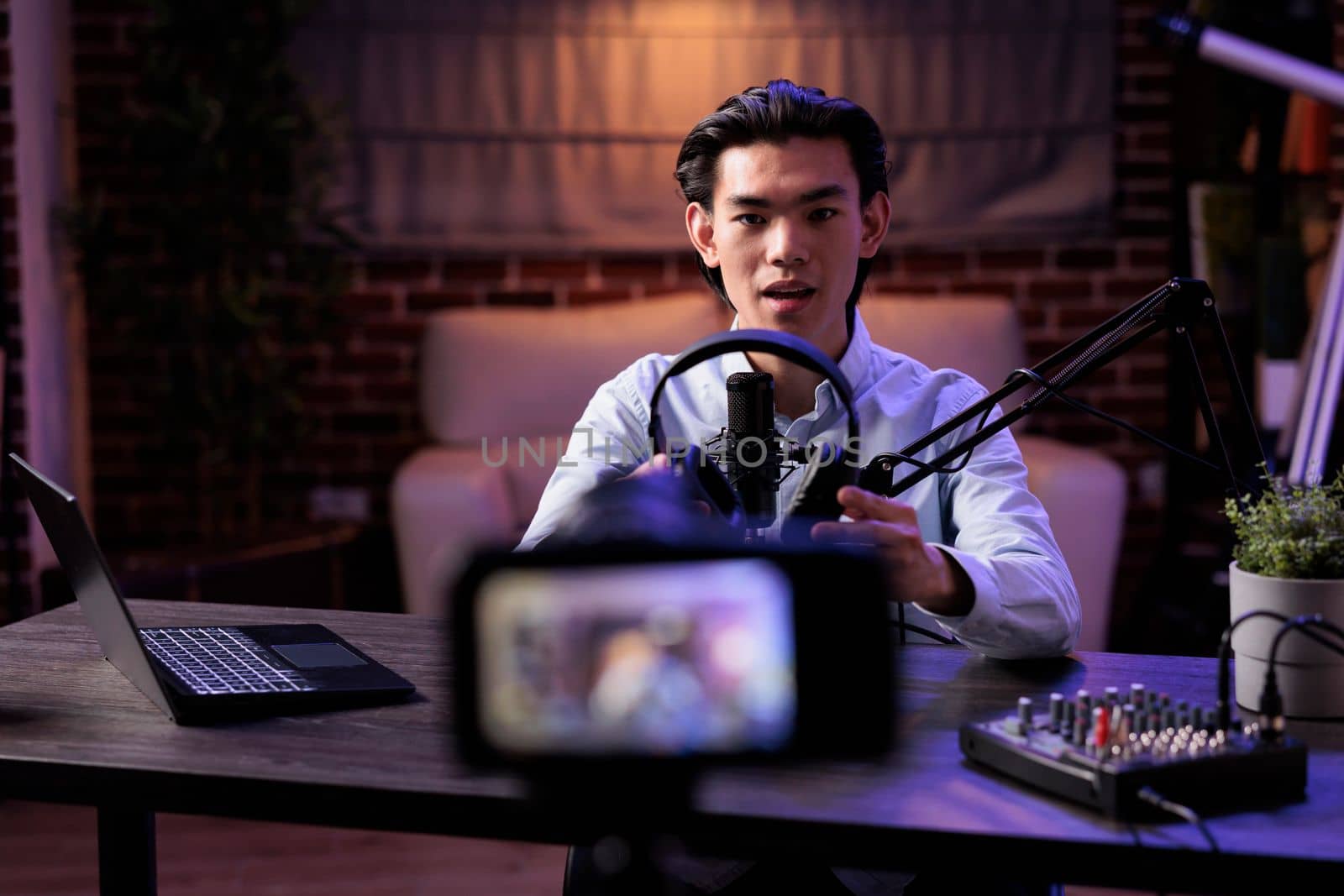 Asian vlogger broadcasting product review with headset on social media channel, recording online vlog and talking about audio headphones. Filming recommendation video with livestreaming station.