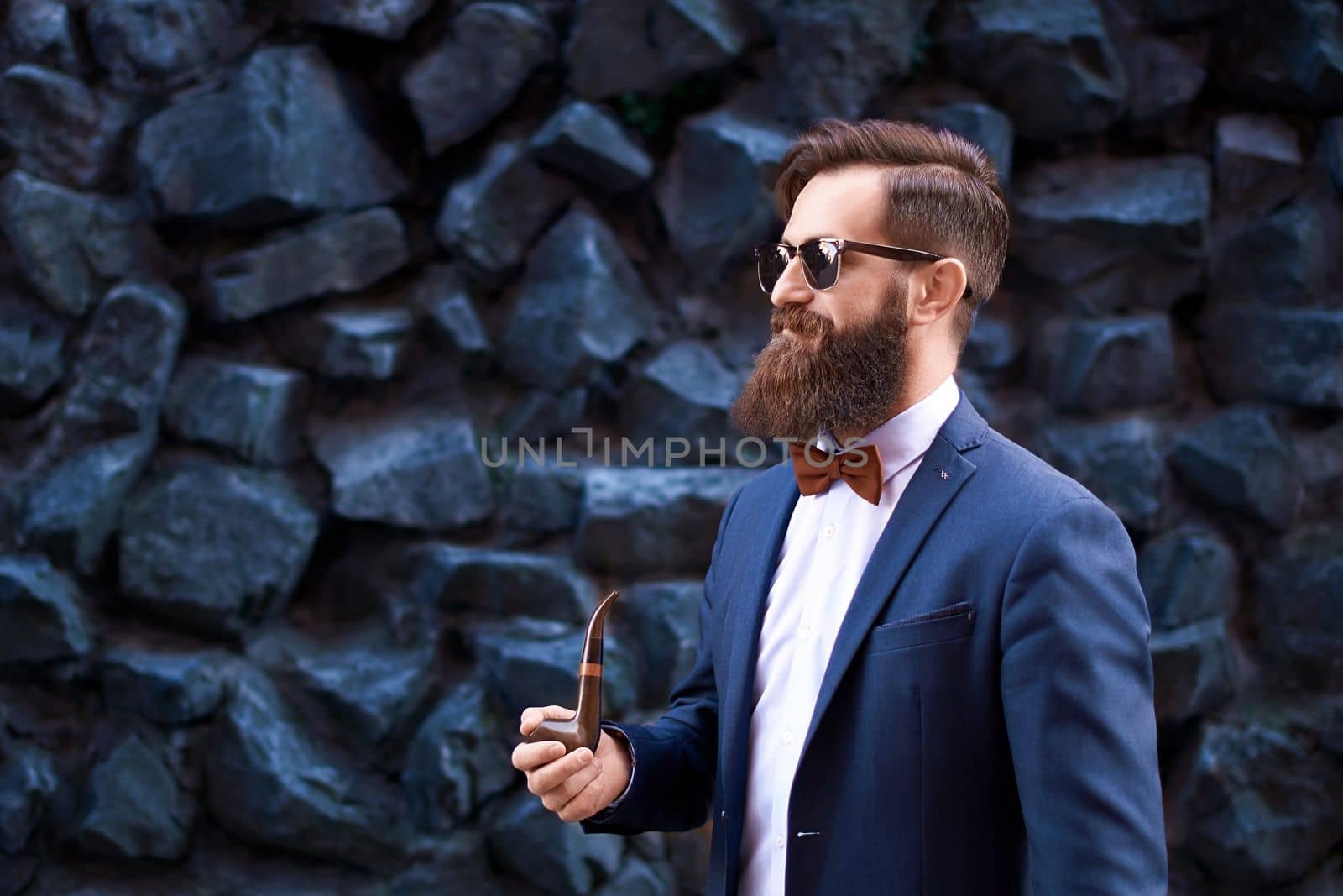 Stylish man with beard wearing a jacket, shirt and bow tie smoking a pipe