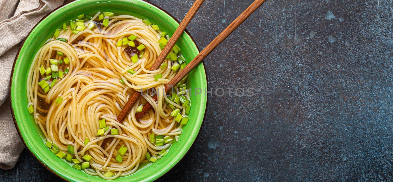 Asian noodles soup in green rustic ceramic bowl with wooden chopsticks top view on rustic stone background. Lo mein noodles bouillon and green onion, space for text by its_al_dente
