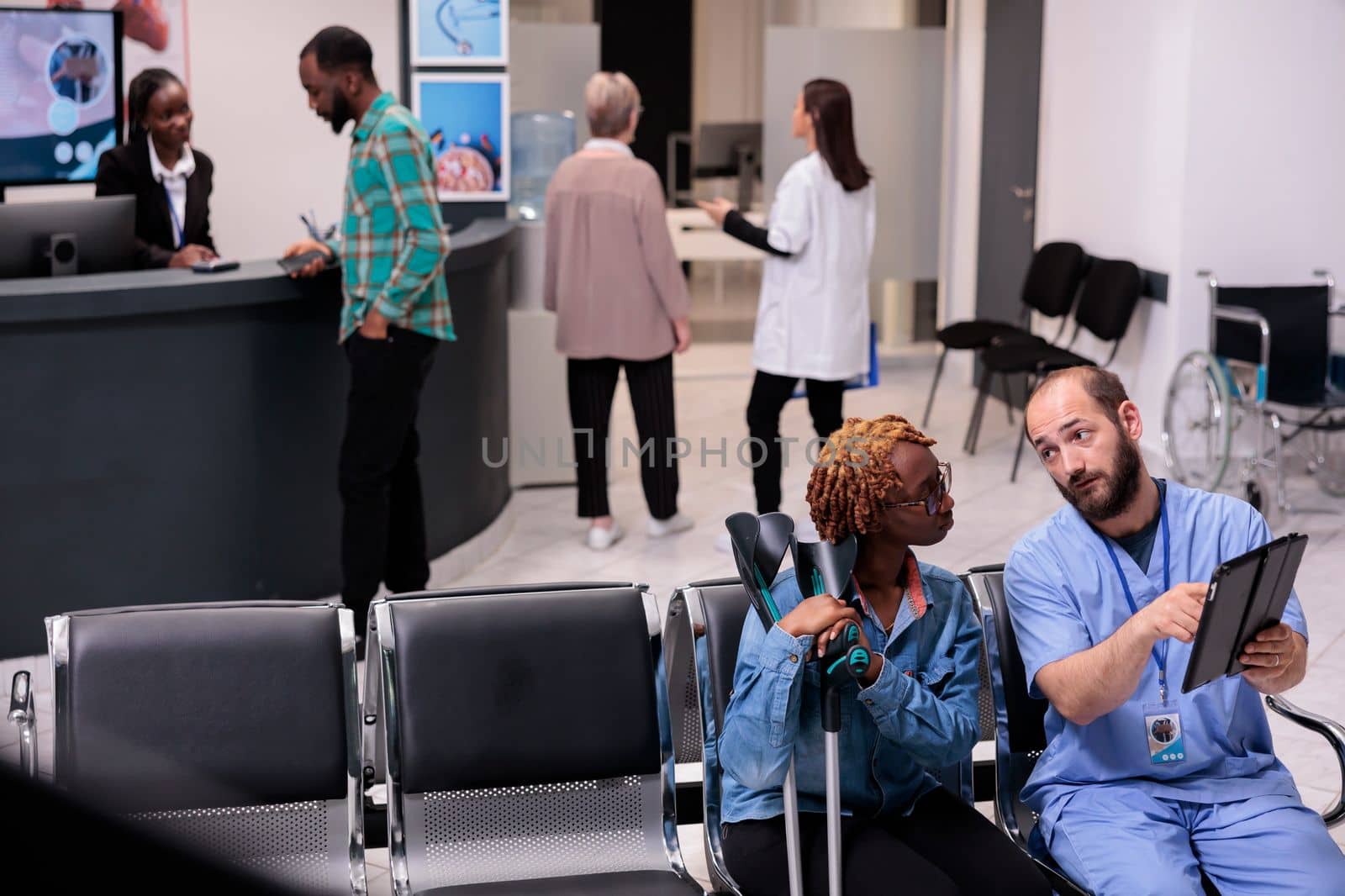 Medical clinic patient reception area filled with multiple nationalities people. African american man requesting patient information at front desk of hospital. Sanatorium staff attending to patients.