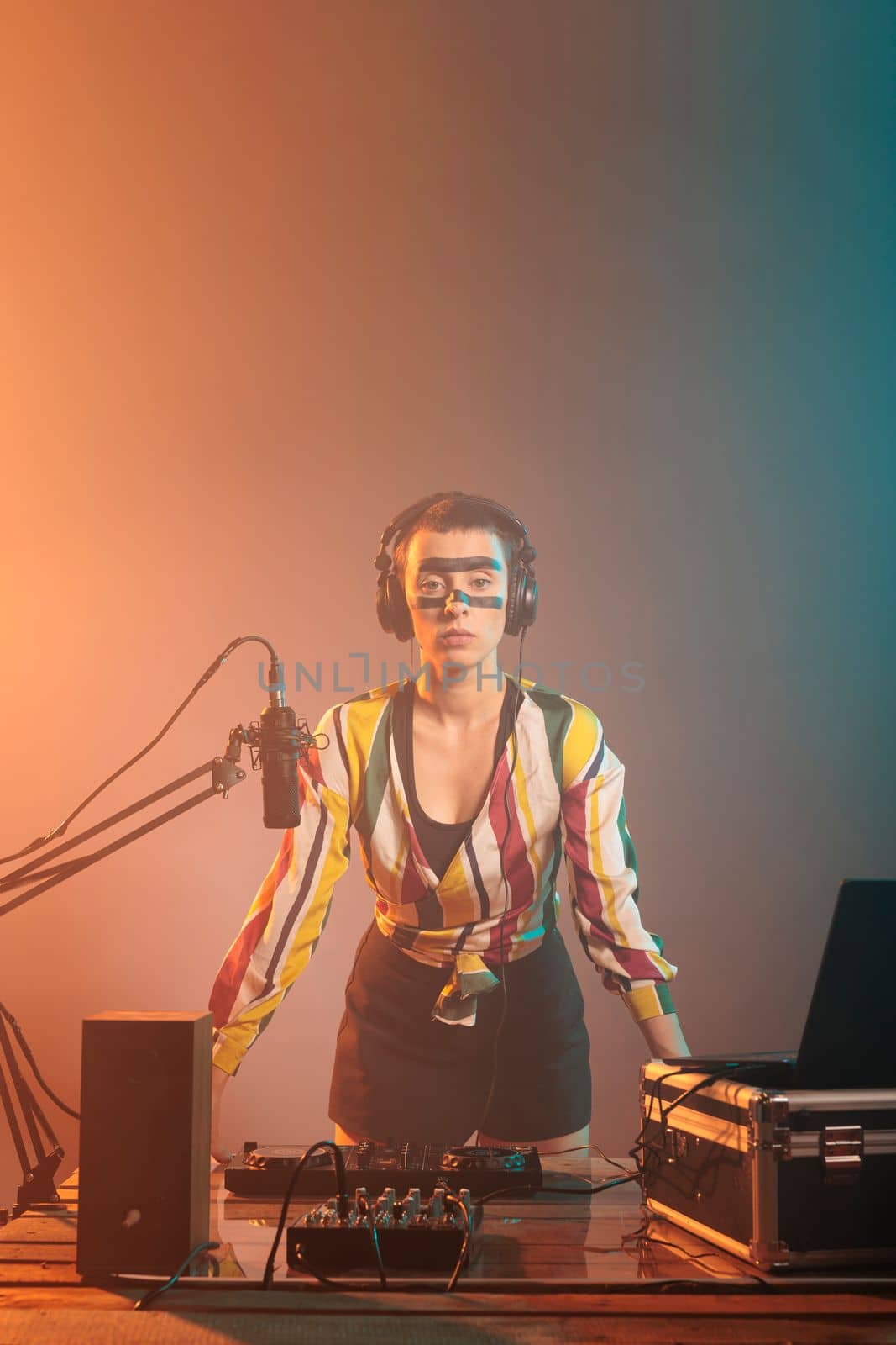 Modern artist standing at turntables and mixing equipment, using audio instruments or mixer to perform techno music. Serious musician with crazy make up doing remix with bass key and buttons.