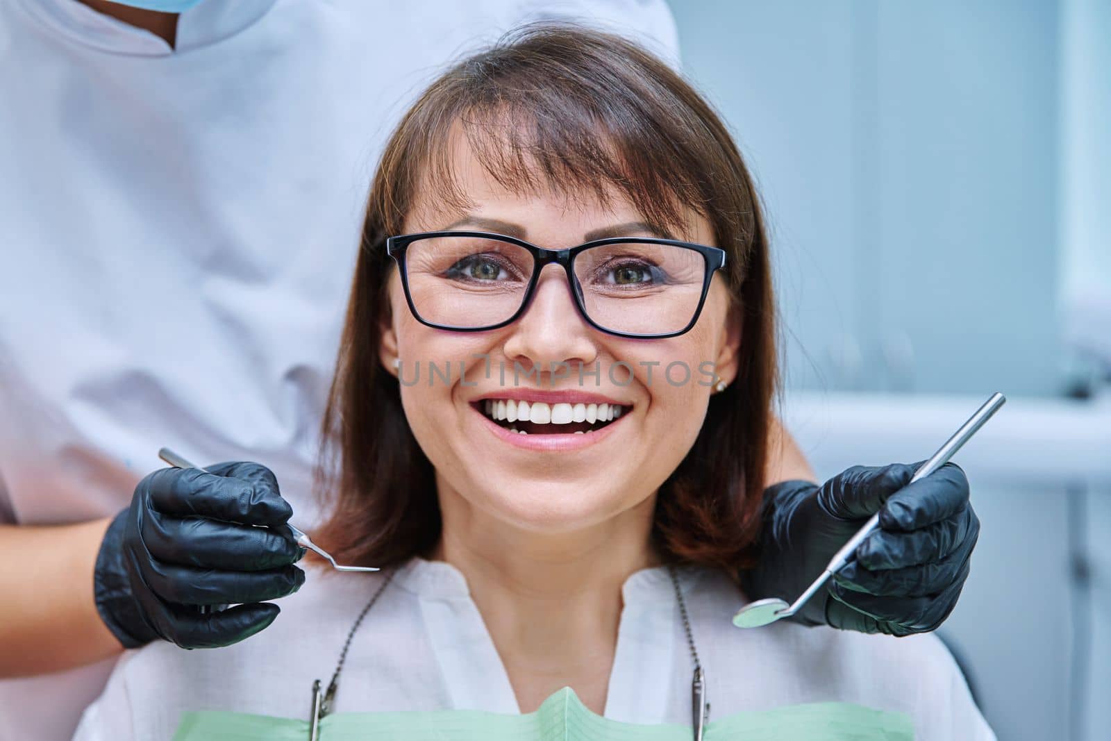 Mature woman with teeth in dentistry with hands with dentist examination tools by VH-studio