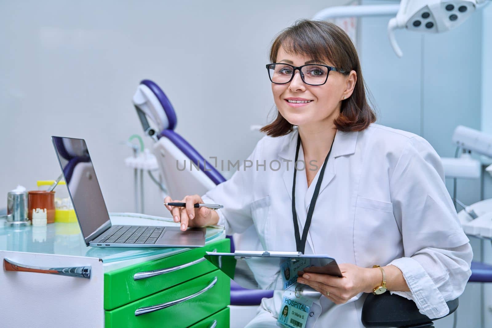 Doctor dentist working in office, using laptop, making notes on clipboard by VH-studio