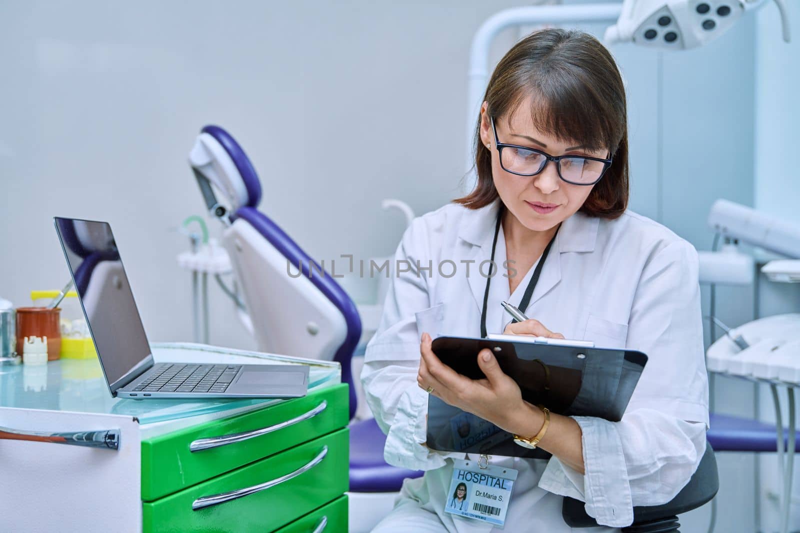 Doctor dentist working in office, using laptop, making notes on clipboard. Dentistry, medicine, hygiene, treatment, dental health care concept