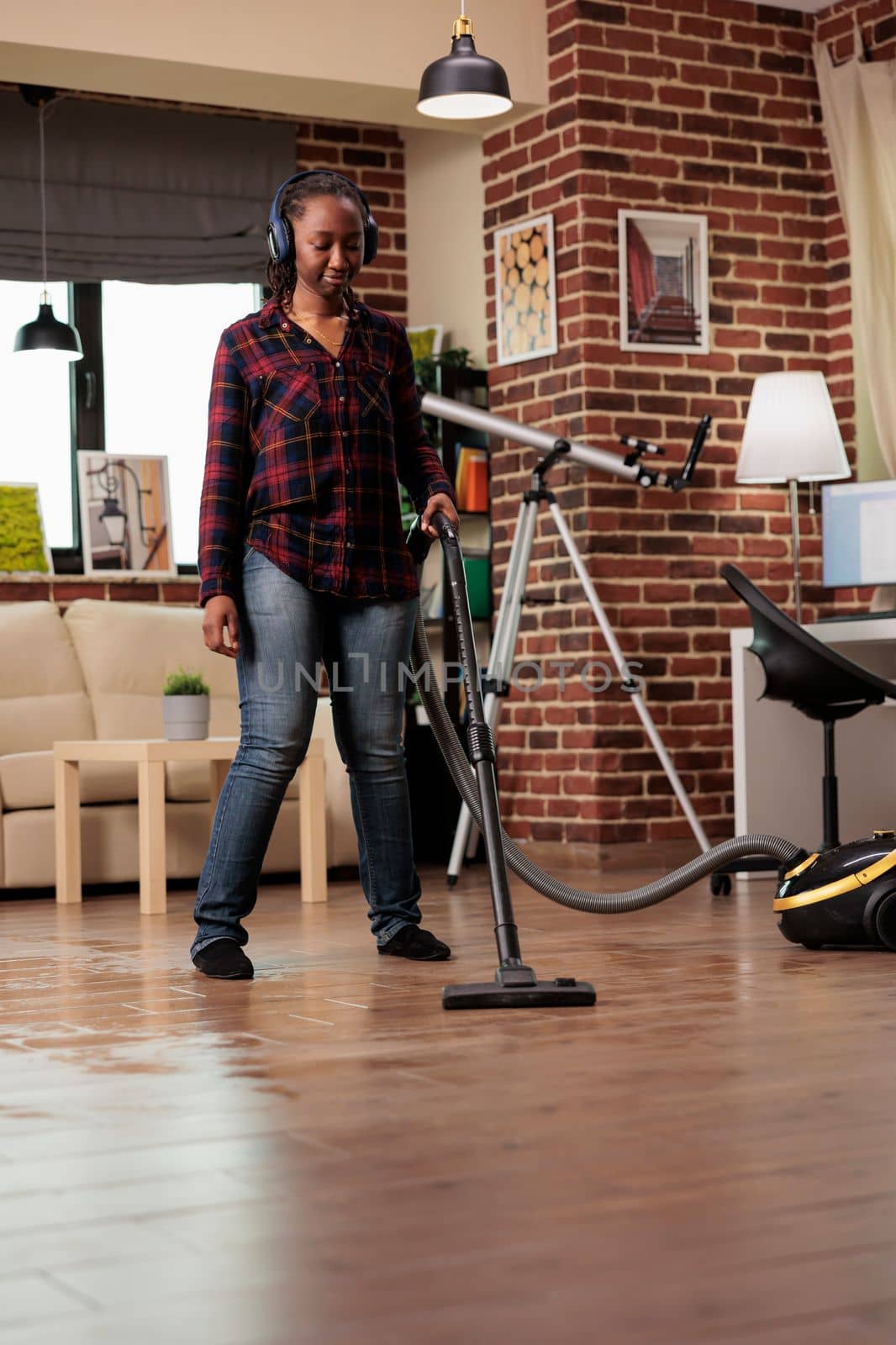 Housewife using modern vacuum cleaner listening to favorite music with wireless headphones. Woman having fun while finishing spring cleaning at home, good vibes and positive energy.