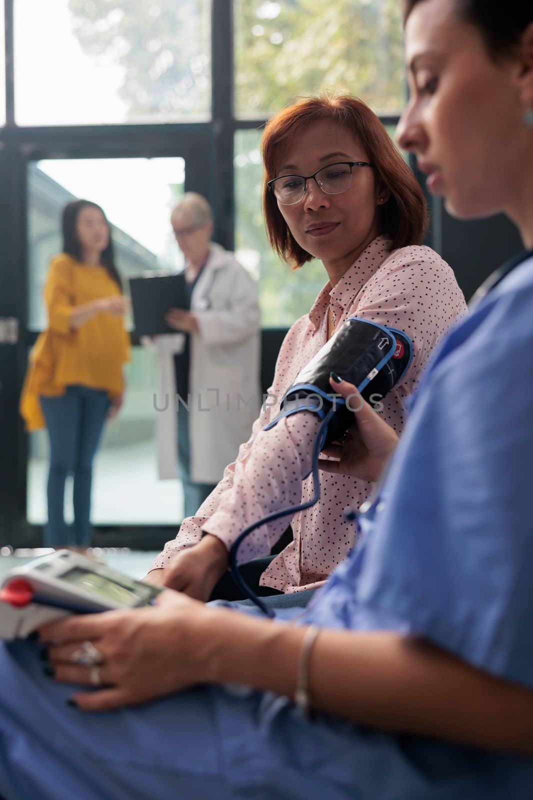 Health specialist measuring hypertension on tonometer in waiting area at health center, checking blood and pulse pressure. Senior patient doing checkup examination with cardiology test.