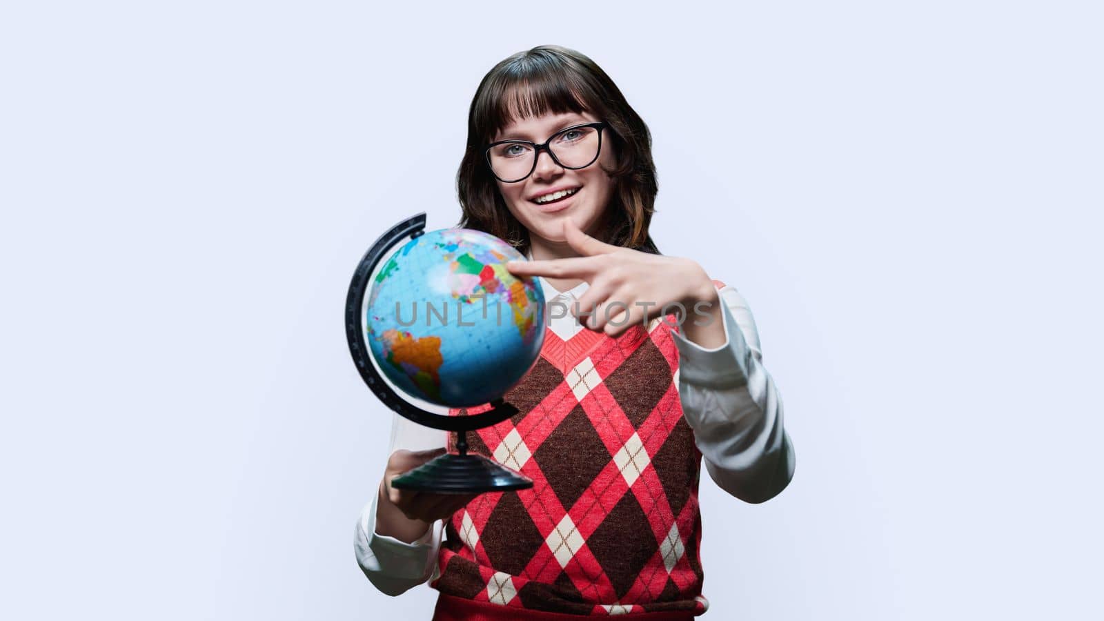 Young female student in glasses holding globe on white studio background, smiling girl looking at camera. Geography, protecting the planet, ecology, travel, education, youth concept