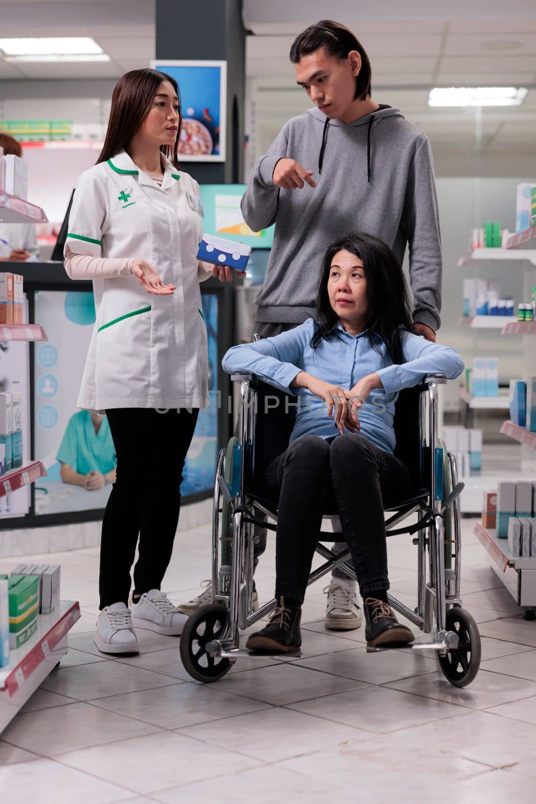 Medical assistant giving pills box to woman and young man, client dealing with chronic disability in pharmacy shop. Asian customers asking pharmacist to help with medicinal supplements.