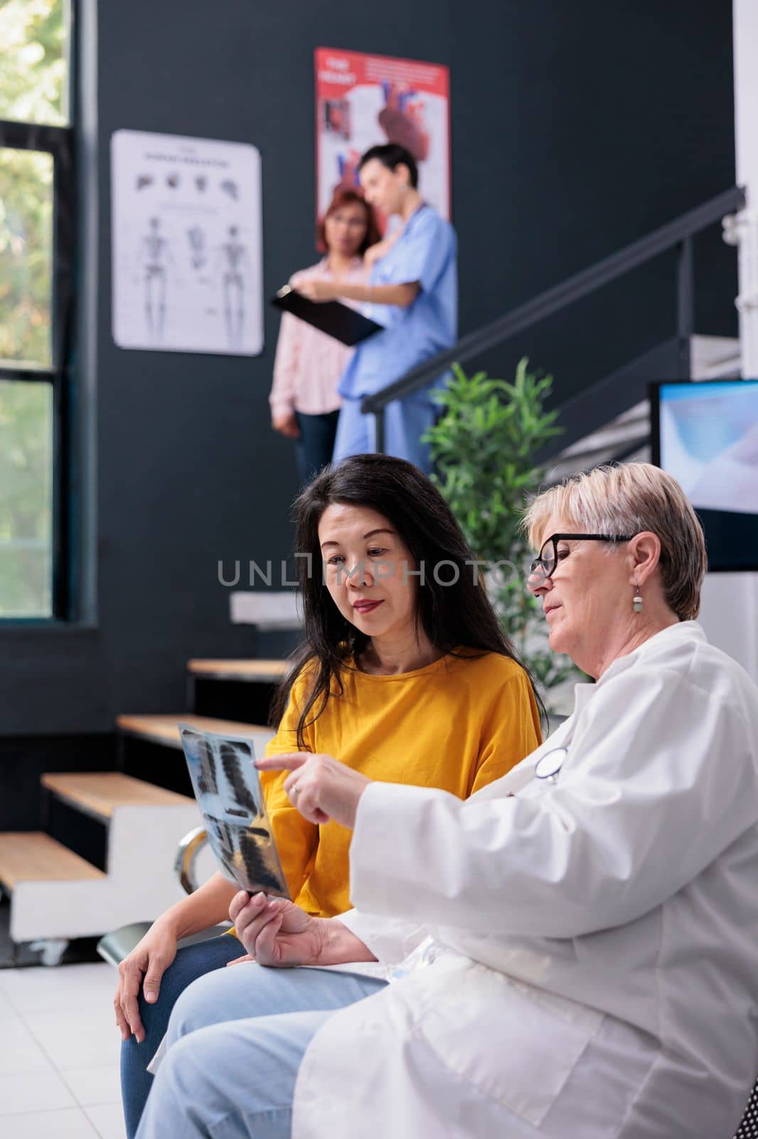 Diverse people looking at bones radiography scan to find medical diagnosis, doctor explaining x ray exam results. Patient attending orthopedic examination with medic in waiting area at clinic.