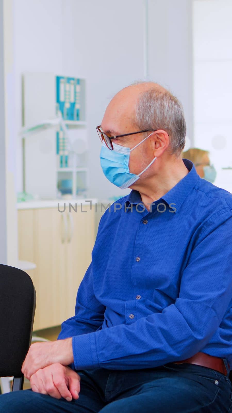 Patients with protection mask talking sitting on chairs keeping social distance in stomatological clinic, waiting for doctor during coronavirus. Concept of new normal dentist visit in covid19 outbreak