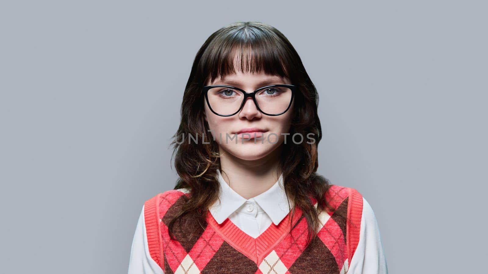 Portrait of confident young female student looking at camera on grey studio background. Serious calm teenage girl 18, 19 years old with glasses. Education, lifestyle, beauty emotion face youth concept