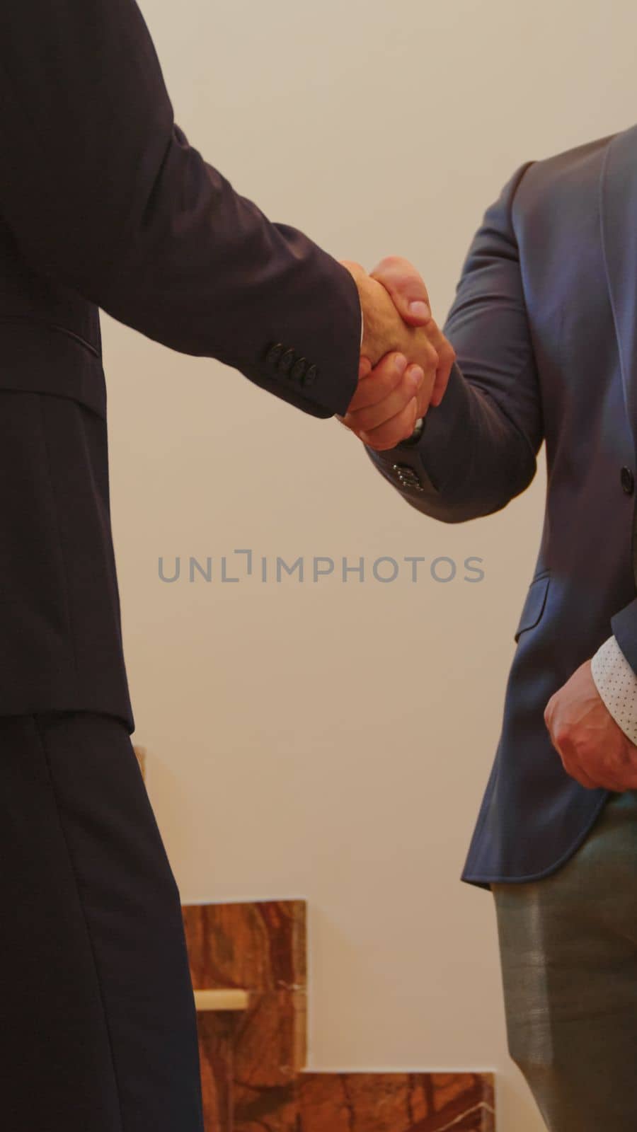 Close up of two business men in suit shaking hands standing on company stairs talking. Group of professional successful businesspeople working in modern financial workplace.