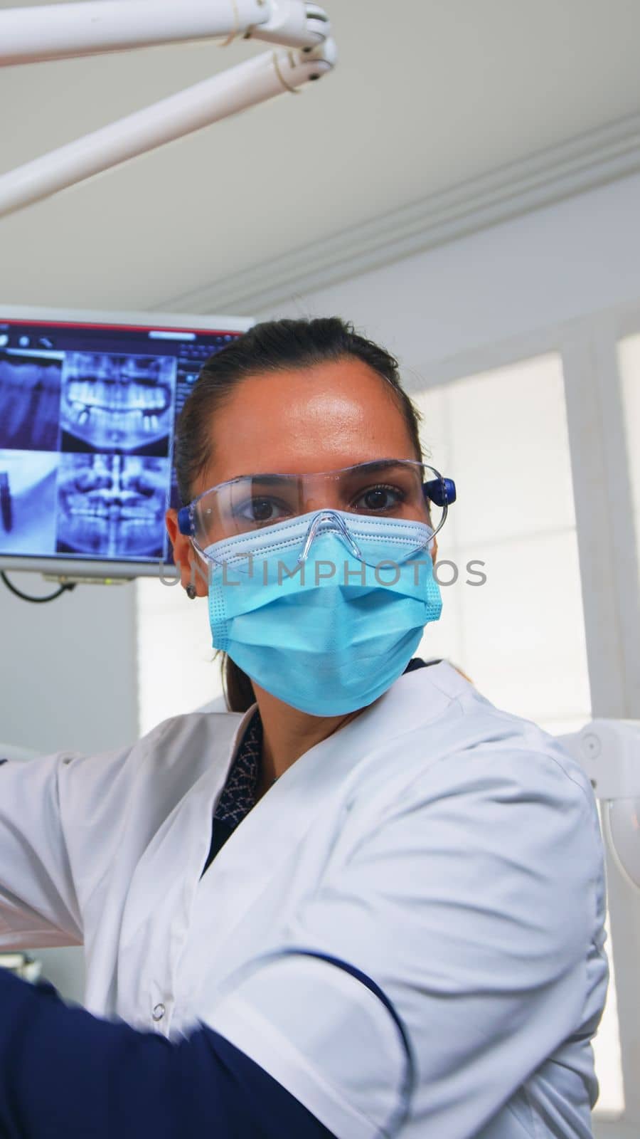 POV of patient in a dental clinic sitting on surgery chair checking affected mass. Dentistry team working in orthodontic office, lighting the lamp and examining person, close-up face in medical mask.