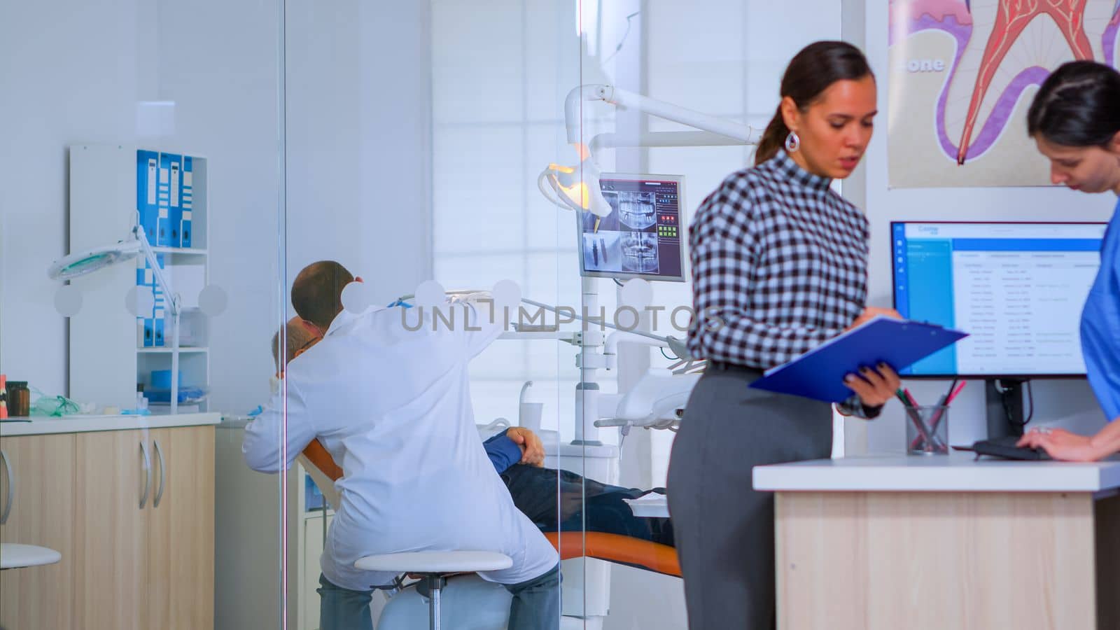 Patients asking for help filling in dental registration form preparing for exemination. Senior woman sitting on chair in waiting area of crowded orthodontist office while doctor working in background