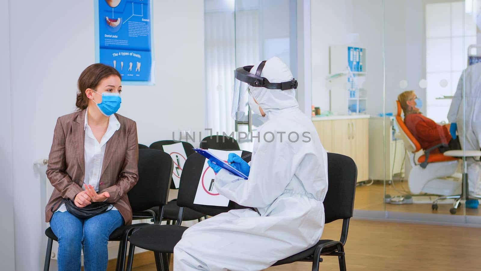 Stomatologist in protective suit reviewing registration form with patient by DCStudio