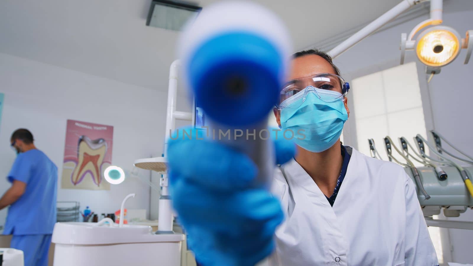 Doctor measuring woman temperature before dental examination, patient pov. Dentist and nurse working in modern orthodontic office, writing and examining person wearing protection mask