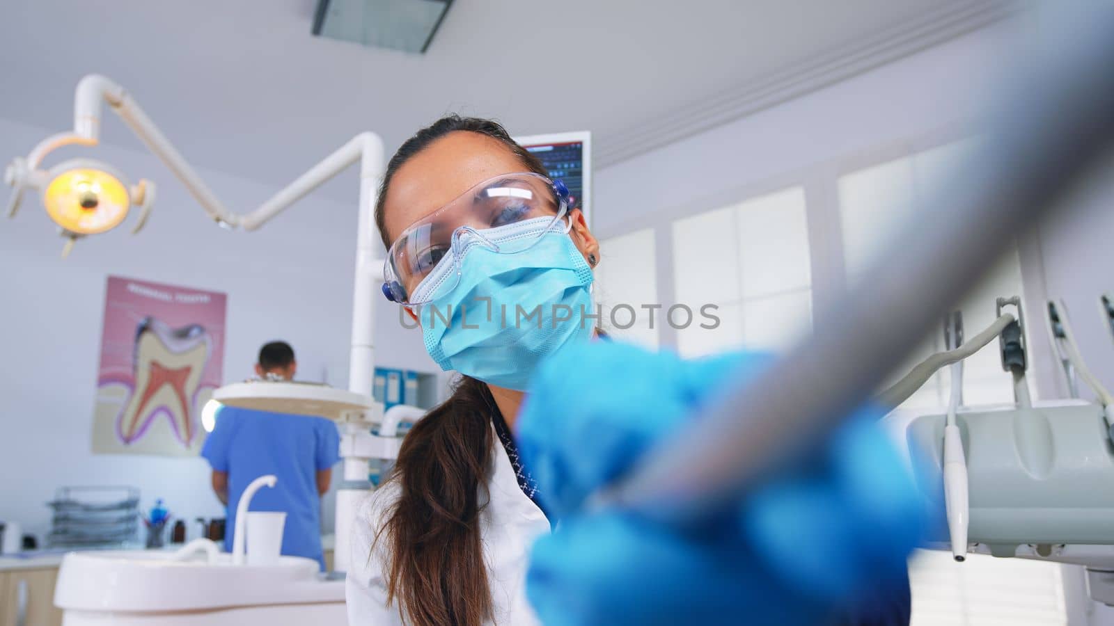 Patient pov to doctor in stomatological office treating teeth of woman. Orthodontic specialist and man assistant working wearing masks and gloves in modern dental clinic.